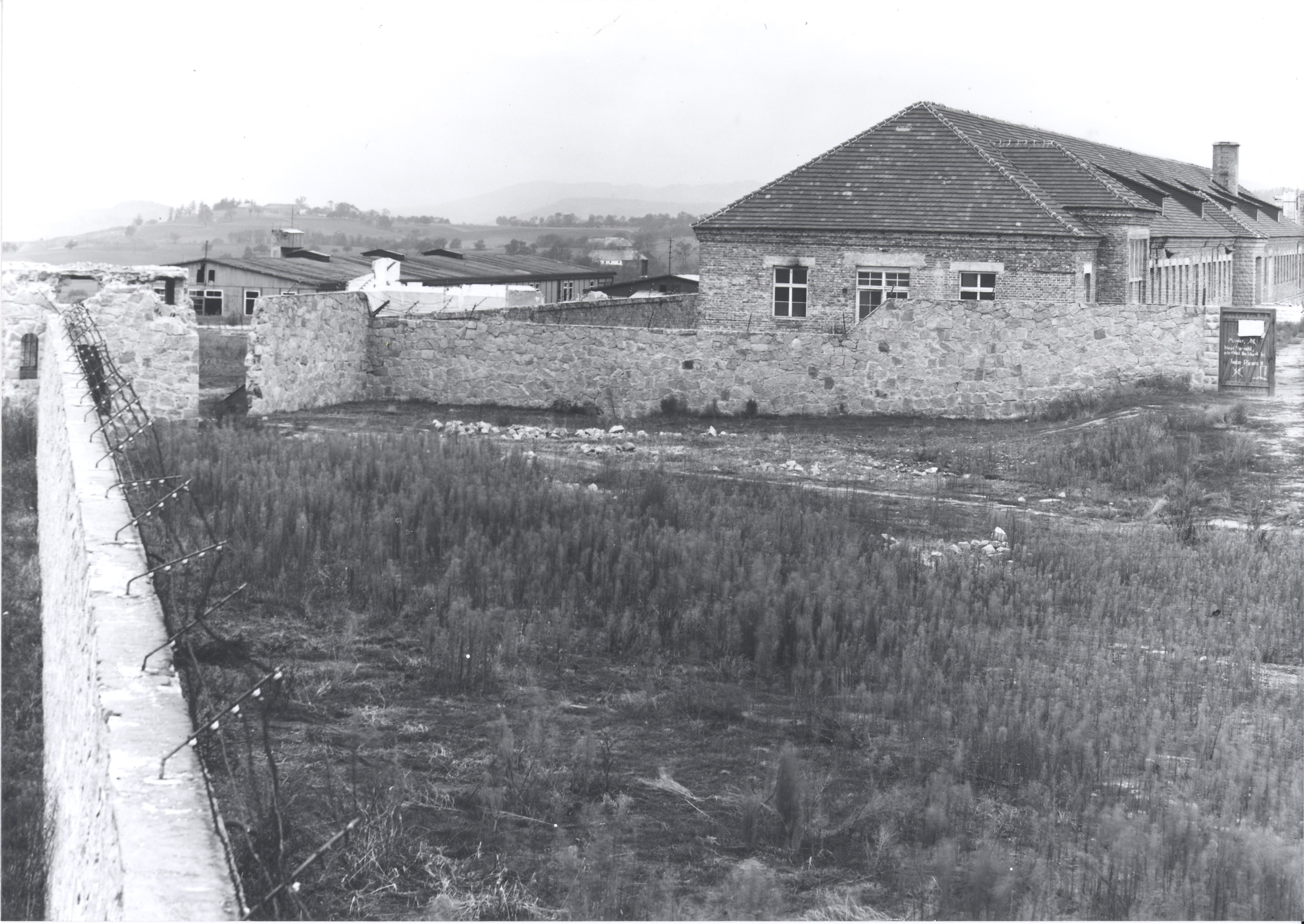 Dieses Foto zeigt die Überreste der Umfassungsmauer des Lagers III. Gut erkennbar ist auch das Reviergebäude, welches ursprünglich nicht verputzt war.
