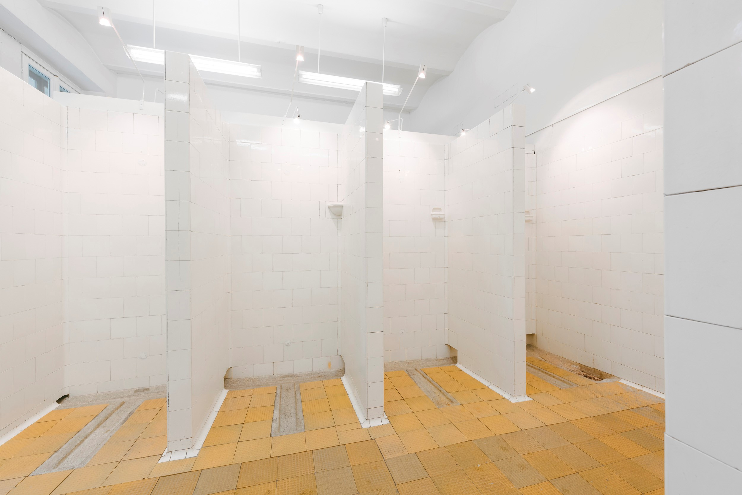 Gefliester Duschraum mit vier offenen Duschzellen im ehemaligen Tröpferlbad